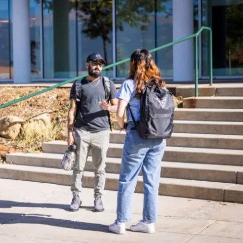 Two students talking in front of a staircase